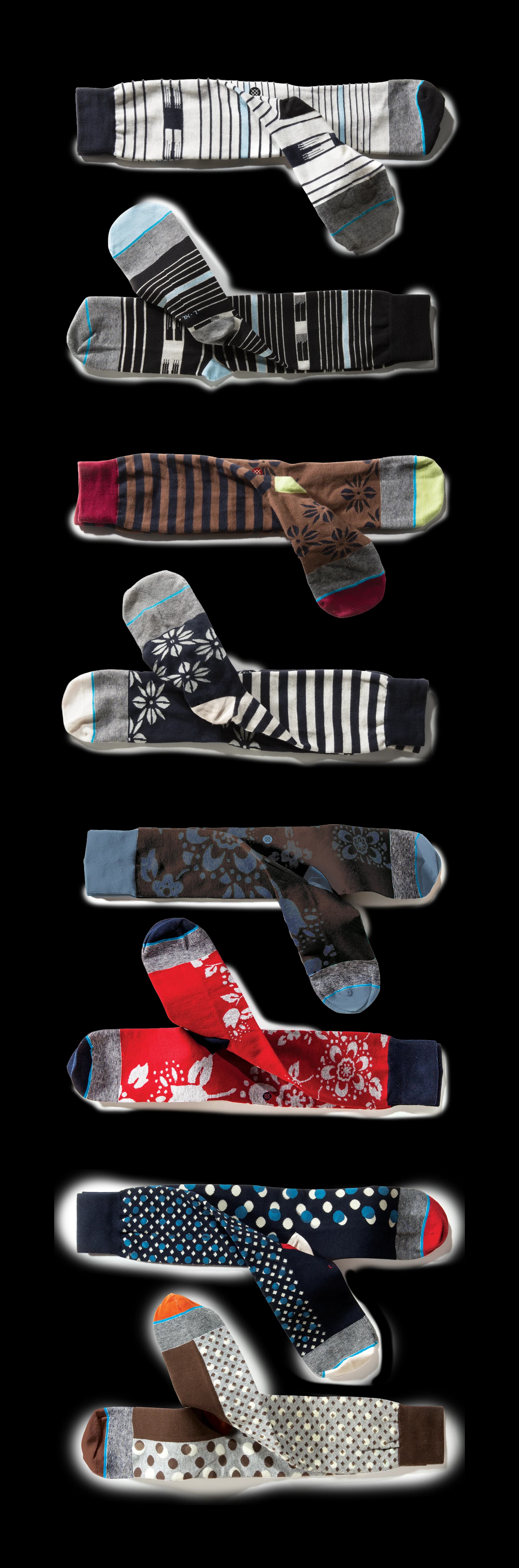 Eight pairs of dress socks laid flat, mixing stripes, florals and polka dots in navy, brown, red and grey.