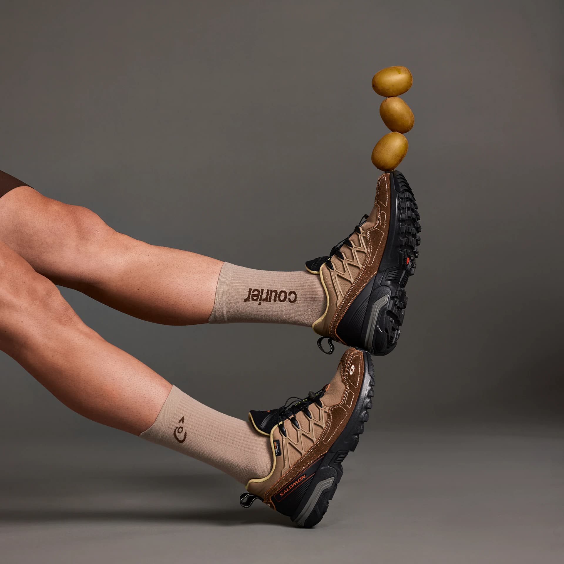 Two legs in Courier socks and hiking shoes, three potatoes balanced on one toe.
