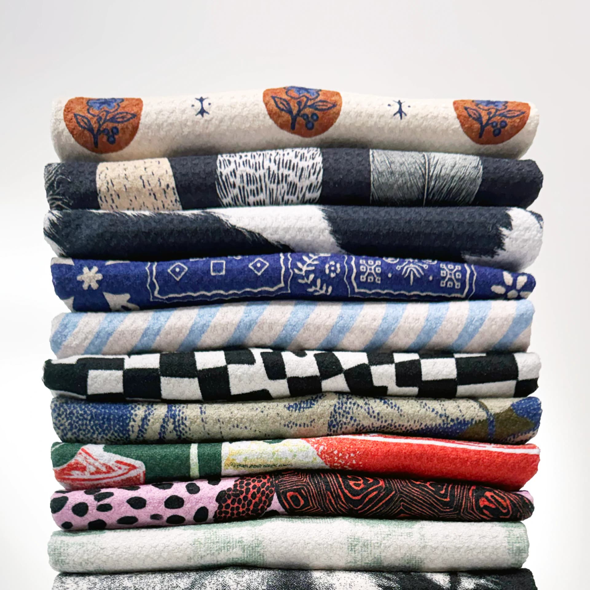 A tall stack of folded towels, each in a different print: florals, checks, stripes, bandana and animal patterns.