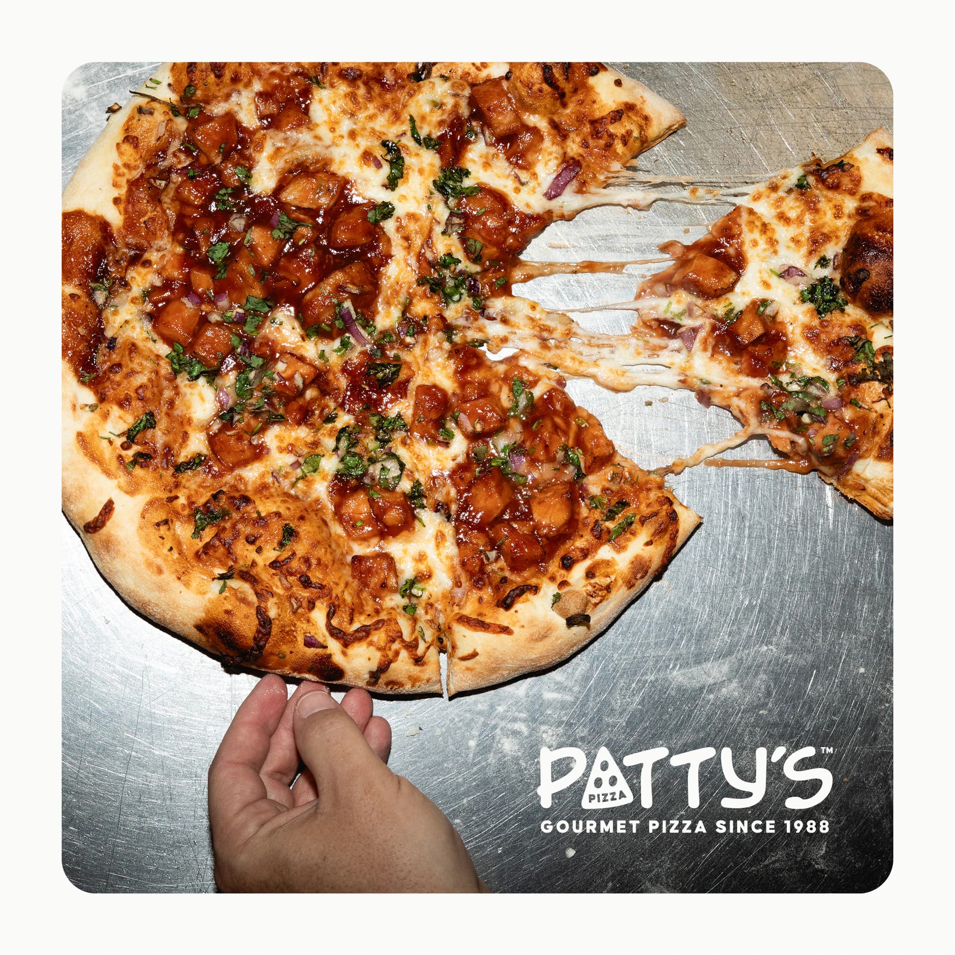 A hand pulling a slice from a barbecue chicken pizza, cheese stretching, with the Patty's logo in the corner.