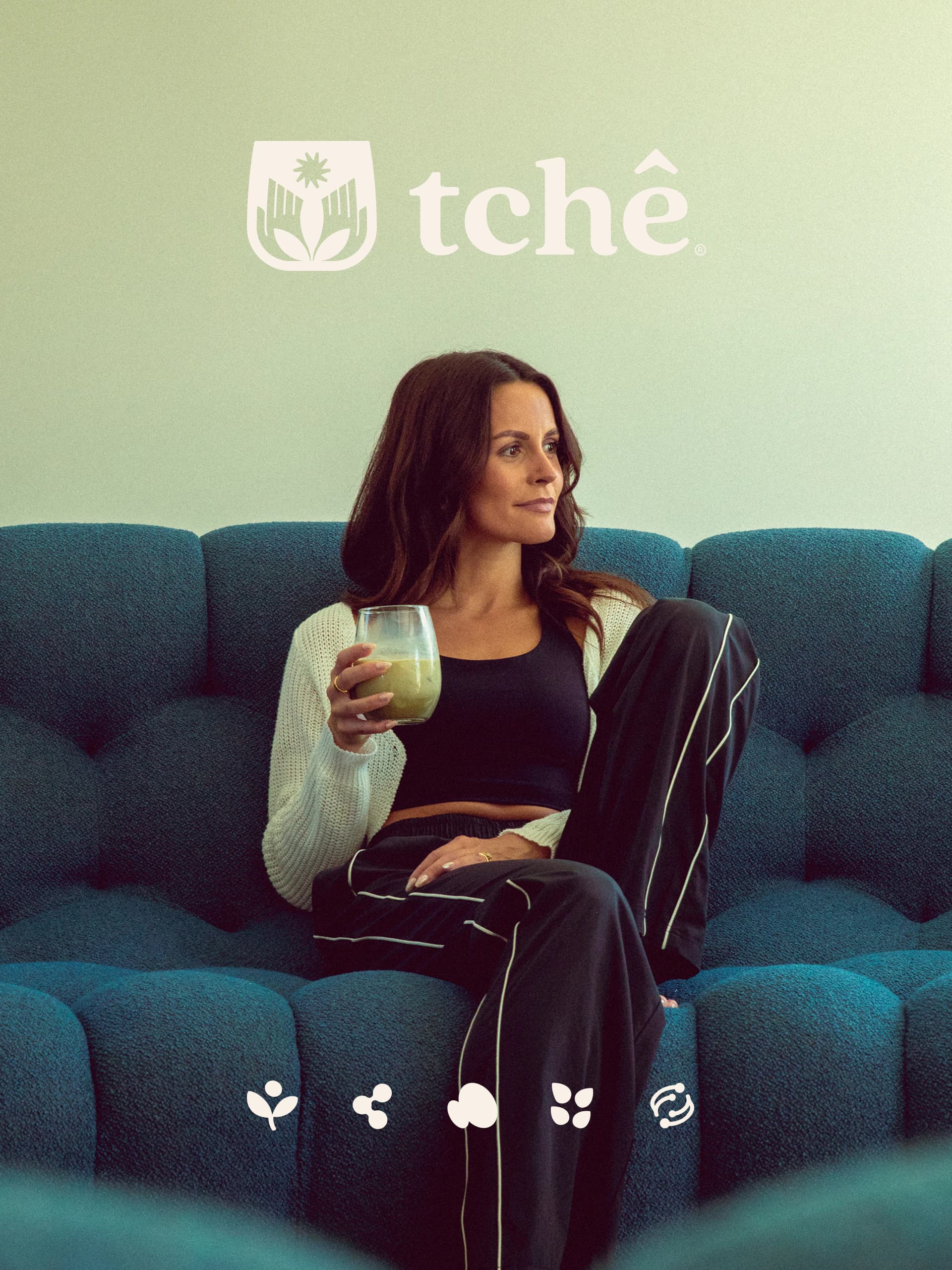 A woman on a teal sofa holding a glass of green Tchê, beneath the Tchê logo and a row of small benefit icons.