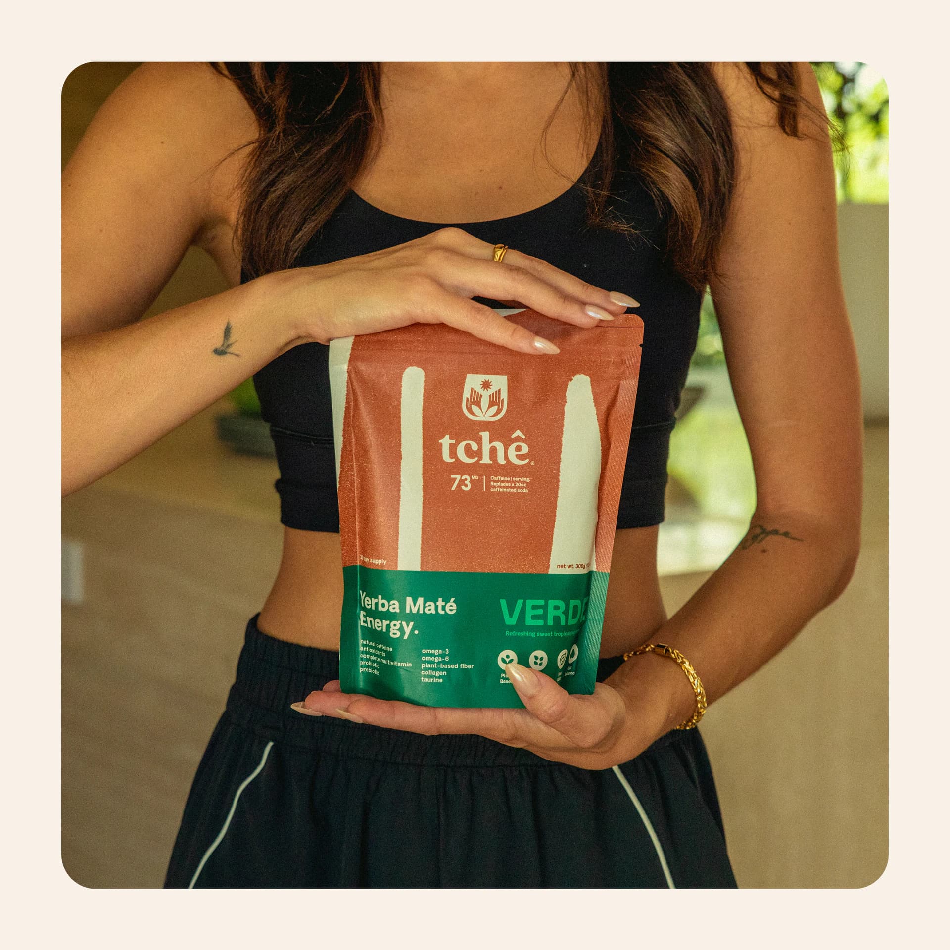 A woman holding a rust-orange Tchê pouch against her waist.